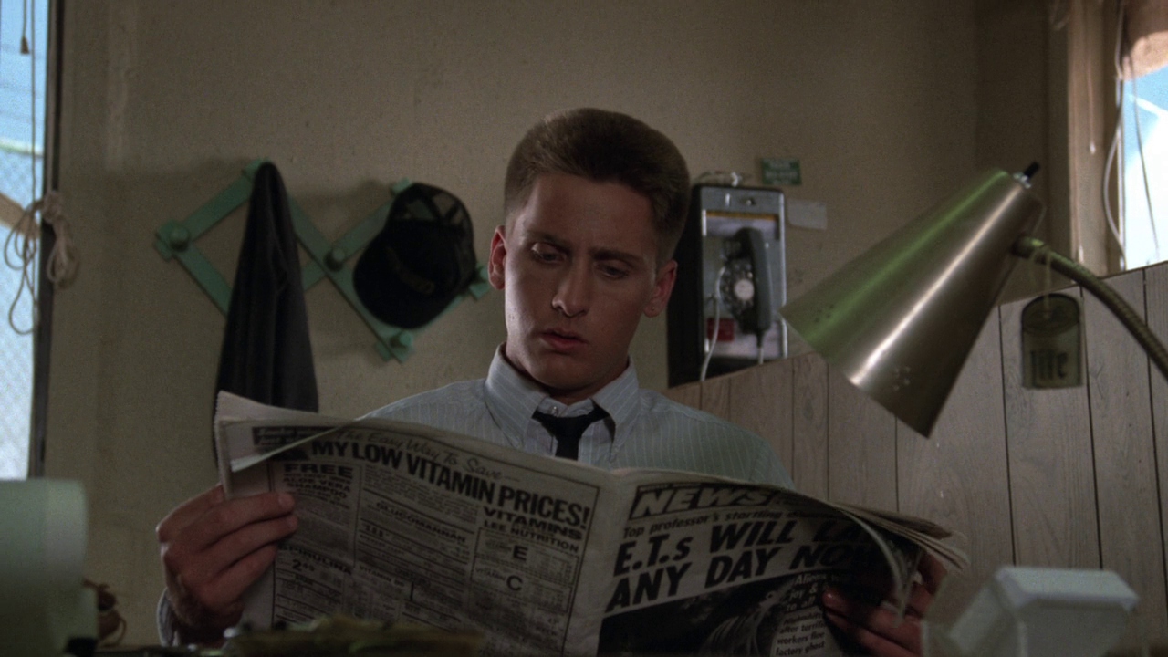 Emilio Estevez reads a newspaper with text about aliens coming and low vitamin prices in Repo Man