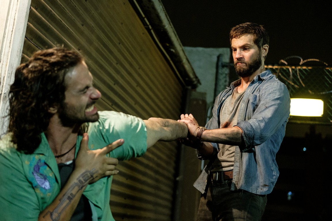 A bearded man in an gray shirt twisting the arm of a man in Upgrade.