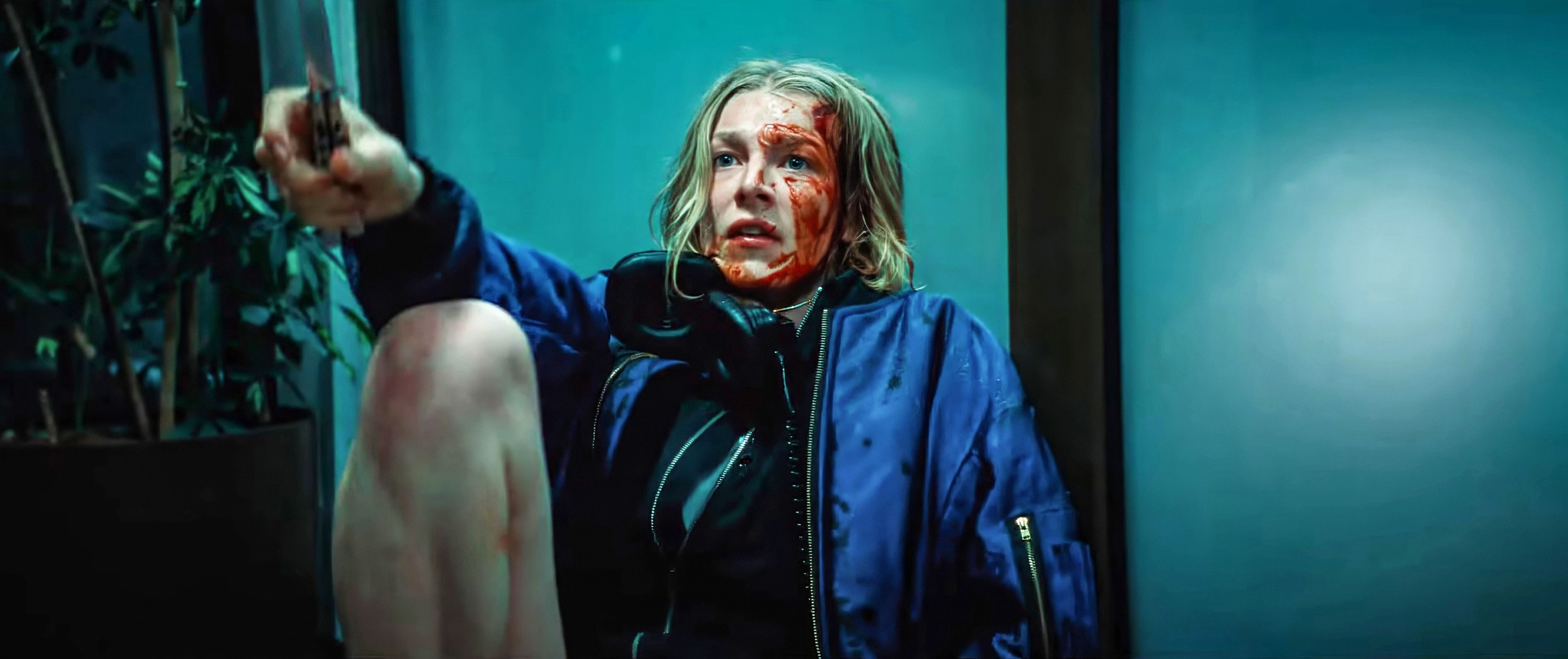 Gretchen (Euphoria’s Hunter Schafer), a teenage girl with her face and hands covered in blood, sits outside against a glass door and waves a knife at an unseen assailant in Tilman Singer’s Cuckoo