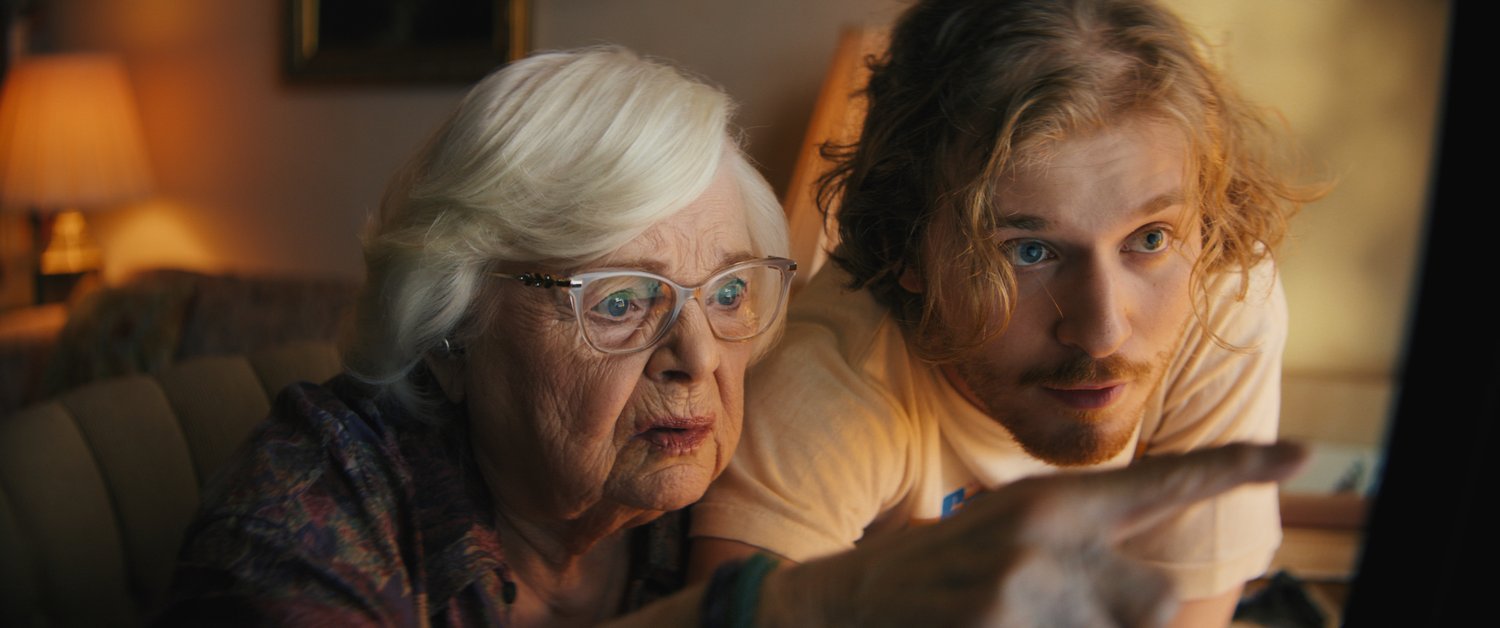 June Squibb and Fred Heschinger in Thelma, sitting closer together looking at a computer screen. 