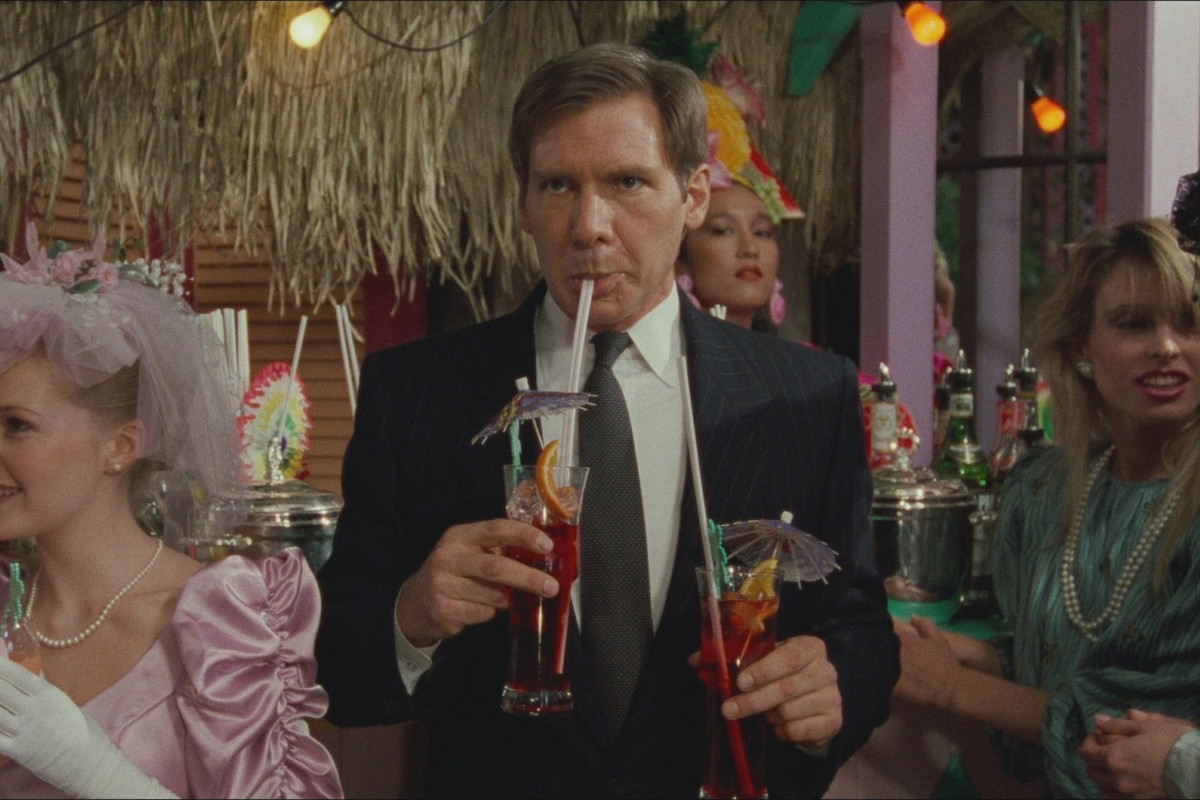 Harrison Ford sips a colorful drinking while holding another one in Working Girl.