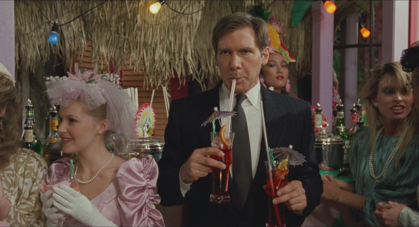 Harrison Ford sips a colorful drinking while holding another one in Working Girl.